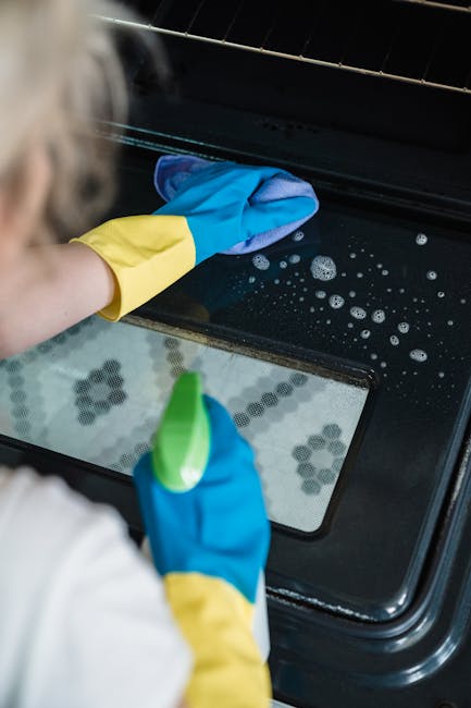 Close-up of a person's hand adjusting the temperature dial on a stainless steel oven in a domestic kitchen setting. The oven front features a digital display showing '20°C' and several control button